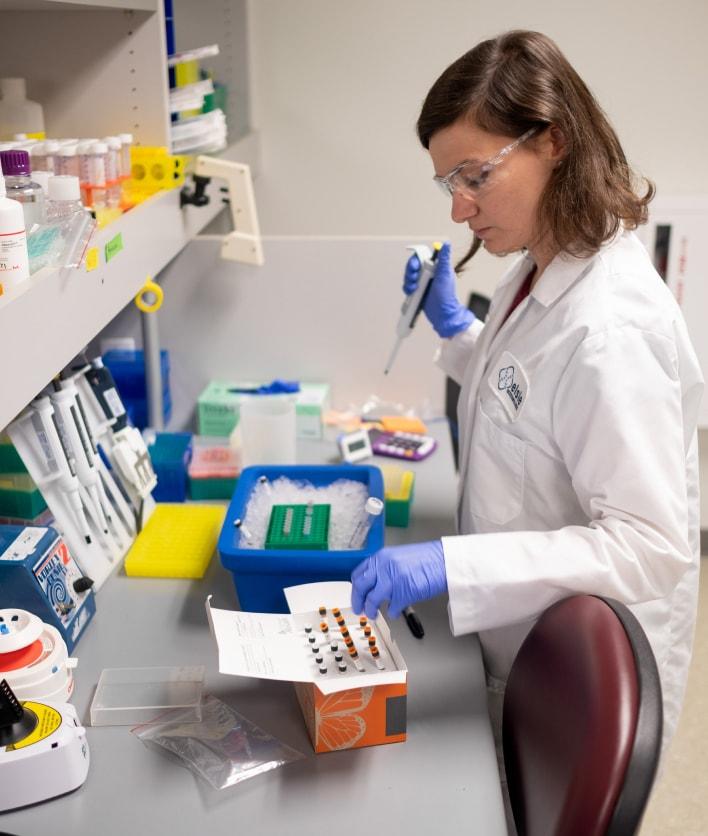 Scientist in lab coat pipetting samples for analysis in a biotechnology laboratory