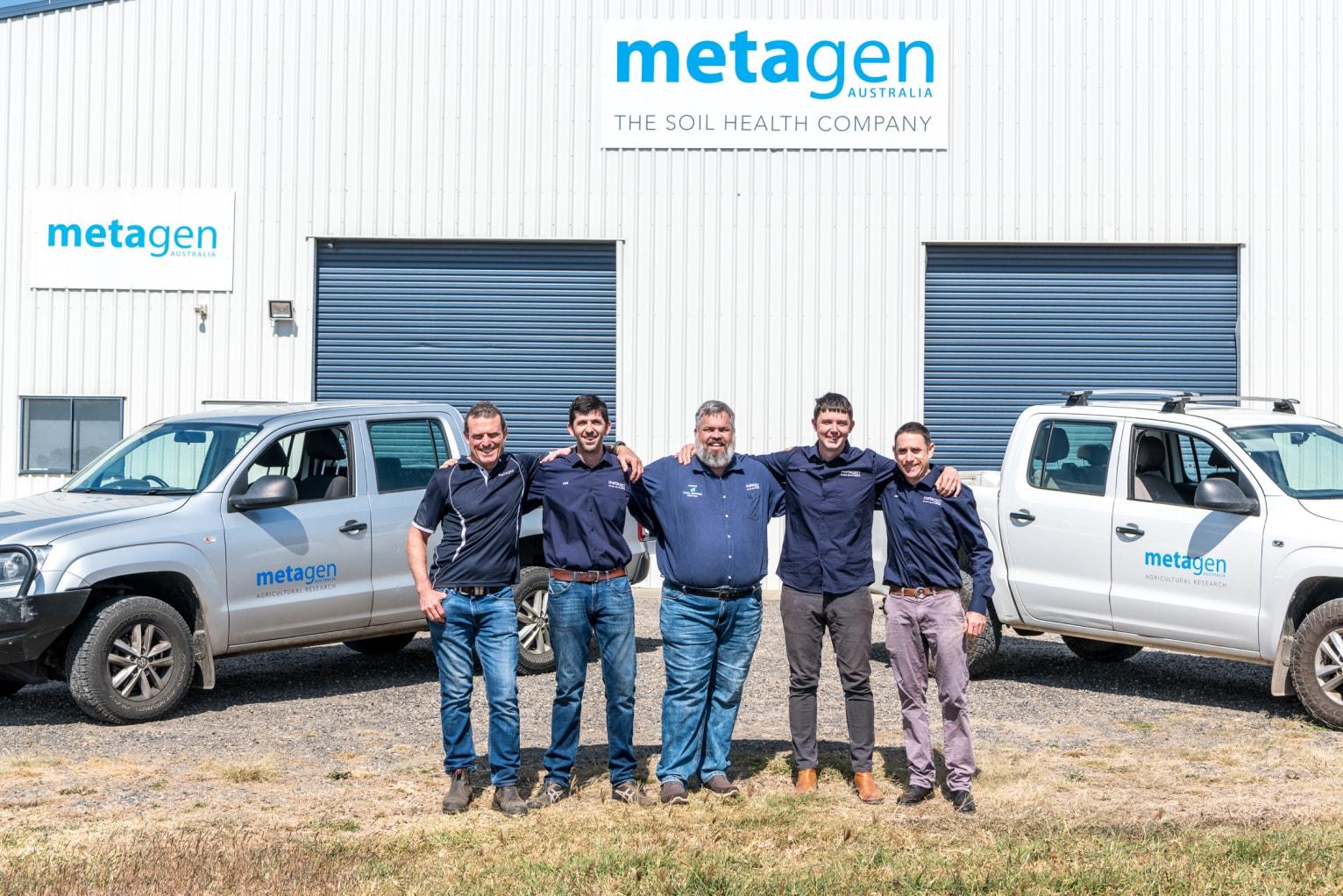 the team at Metagen posing outside of a large garage building with a sign that says 'Metagen'